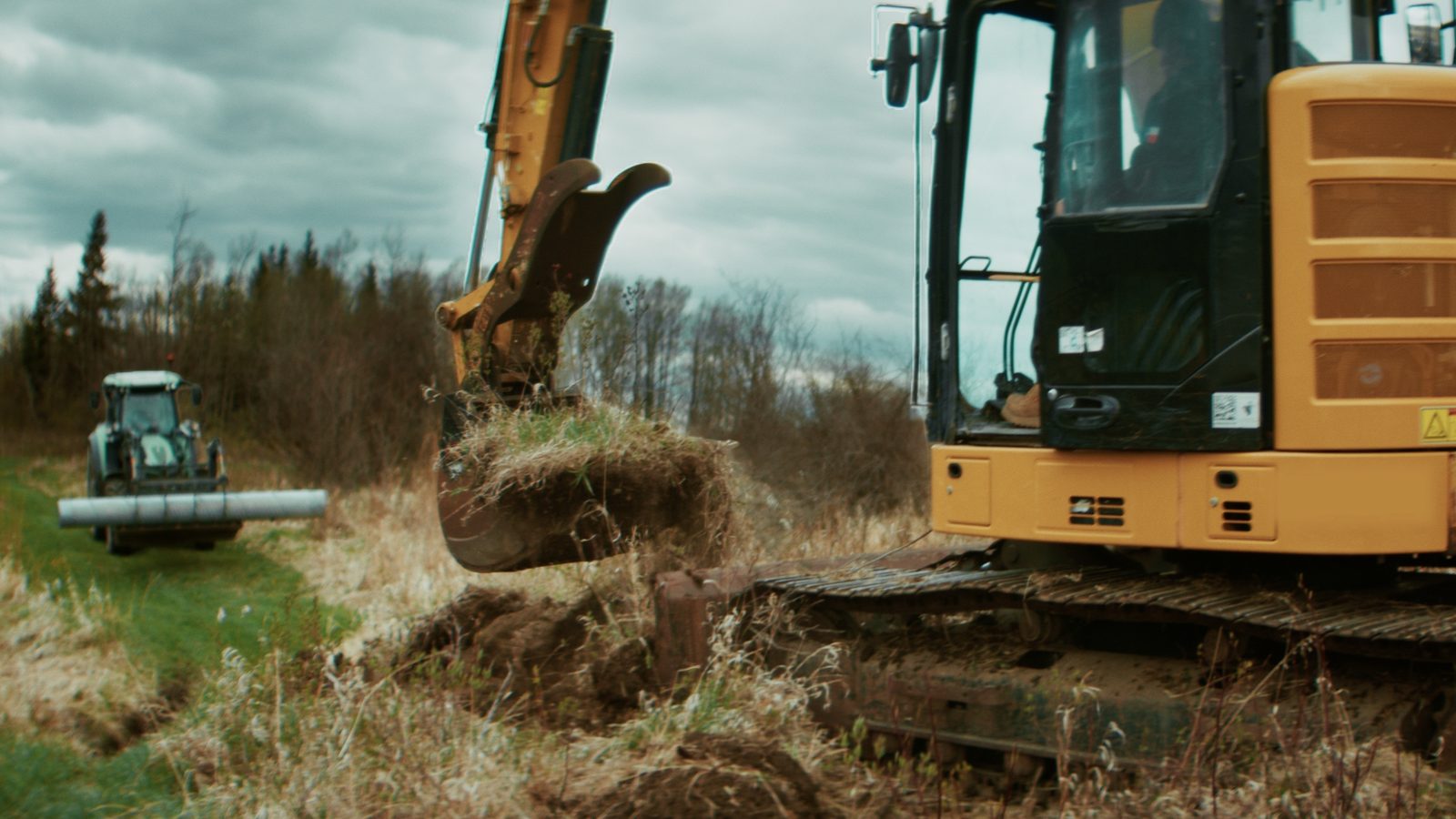 Excavator installing a culvert next to a tractor on a Red Deer County property